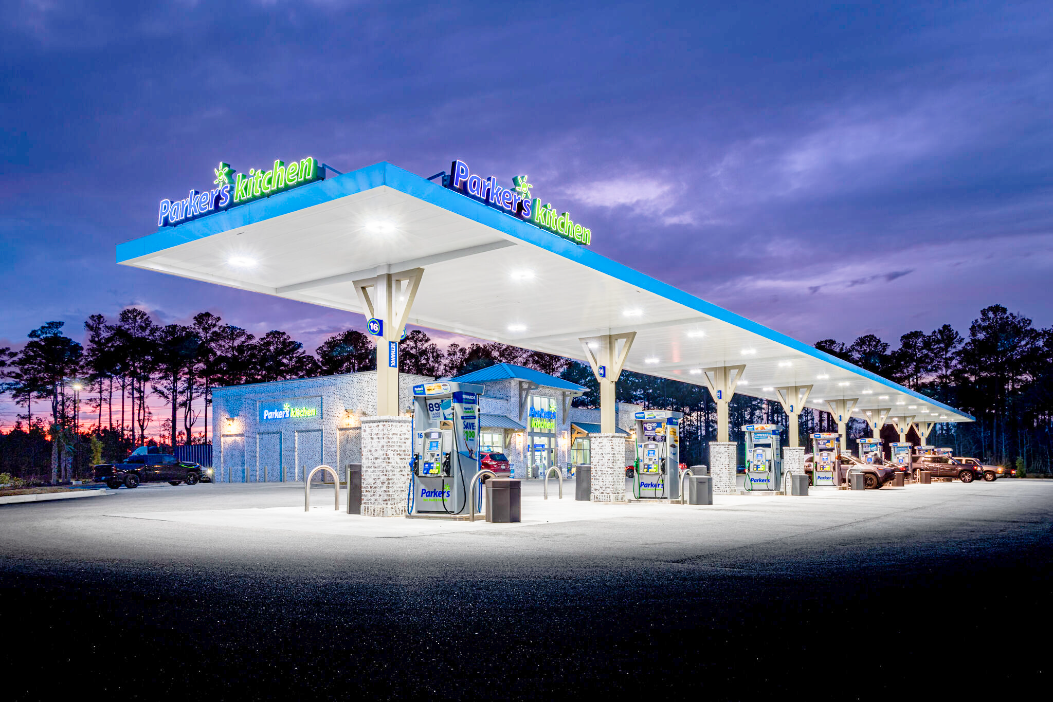 Parker's Kitchen gas station canopy lit at dusk with fueling pumps and cars nearby.